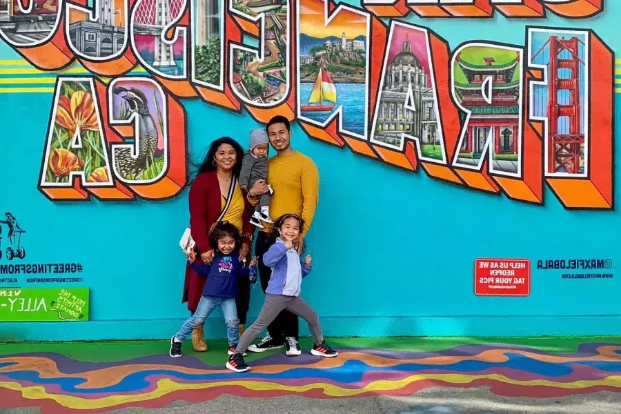 Uma família posando para uma foto em frente a um mural de São Francisco